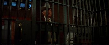Movie still from “The Getaway” (1972), directed by Sam Peckinpah – A man in a suit and hat behind bars; Medium shot, Low angle