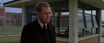 Movie still from “The Getaway” (1972), directed by Sam Peckinpah – A man in a suit and tie standing in front of a building; Medium shot, Over the shoulder angle