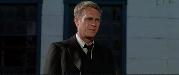 Movie still from “The Getaway” (1972), directed by Sam Peckinpah – A man in a suit and tie standing in front of a building; Close Up shot, Over the shoulder angle