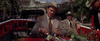 Movie still from “The Getaway” (1972), directed by Sam Peckinpah – A man wearing a cowboy hat is cutting a piece of cake; Medium shot, Over the shoulder angle