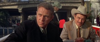 Movie still from “The Getaway” (1972), directed by Sam Peckinpah – A man in a suit and tie looking at the camera; Medium shot, Over the shoulder angle
