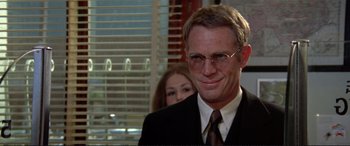 Movie still from “The Getaway” (1972), directed by Sam Peckinpah – A man in a suit and tie with a woman behind him; Close Up shot, Over the shoulder angle