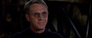 Movie still from “The Getaway” (1972), directed by Sam Peckinpah – A person wearing glasses and a black shirt; Close Up shot, Over the shoulder angle