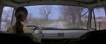 Movie still from “The Getaway” (1972), directed by Sam Peckinpah – A man driving a car down a rural road; Wide shot, Over the shoulder angle