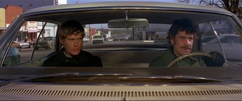 Movie still from “The Getaway” (1972), directed by Sam Peckinpah – Two men in the back seat of a car looking out the window; Medium shot, Over the shoulder angle