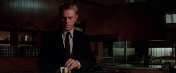 Movie still from “The Getaway” (1972), directed by Sam Peckinpah – A man in a suit and tie holding a cup of coffee; Medium shot, Low angle