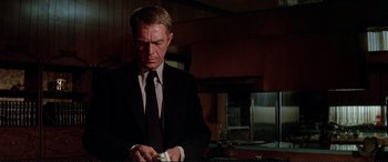 Movie still from “The Getaway” (1972), directed by Sam Peckinpah – A man in a suit and tie holding something in his hands; Medium shot, Low angle