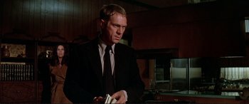 Movie still from “The Getaway” (1972), directed by Sam Peckinpah – A man in a suit and tie holding a stack of papers; Medium shot, Low angle