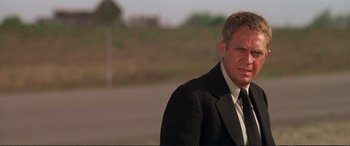 Movie still from “The Getaway” (1972), directed by Sam Peckinpah – A man in a suit and tie standing in front of a road; Close Up shot, Low angle