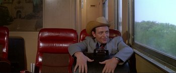 Movie still from “The Getaway” (1972), directed by Sam Peckinpah – A man in a cowboy hat sitting in a chair with a briefcase; Medium shot, Over the shoulder angle