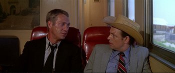Movie still from “The Getaway” (1972), directed by Sam Peckinpah – Two men sitting next to each other on a red chair; Medium shot, Over the shoulder angle