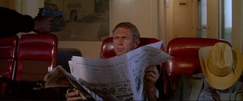 Movie still from “The Getaway” (1972), directed by Sam Peckinpah – A man sitting in a red chair reading a newspaper; Close Up shot, Over the shoulder angle