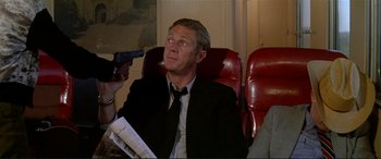 Movie still from “The Getaway” (1972), directed by Sam Peckinpah – A man in a suit and tie holding a gun; Medium shot, Over the shoulder angle