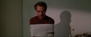 Movie still from “The Getaway” (1972), directed by Sam Peckinpah – A man wrapped in white tape with his head down; Medium shot, High angle