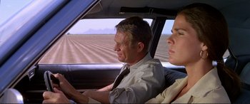 Movie still from “The Getaway” (1972), directed by Sam Peckinpah – A man and a woman driving a car in a field; Medium shot, Over the shoulder angle
