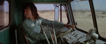 Movie still from “The Getaway” (1972), directed by Sam Peckinpah – A man driving a truck in the middle of the desert; Medium shot, Low angle