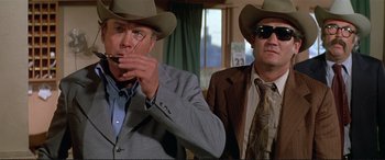 Movie still from “The Getaway” (1972), directed by Sam Peckinpah – Two men wearing cowboy hats and smoking a cigarette; Medium shot, Low angle