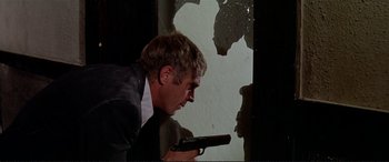 Movie still from “The Getaway” (1972), directed by Sam Peckinpah – A man holding a gun while standing in front of a broken window; Medium shot, Low angle