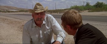 Movie still from “The Getaway” (1972), directed by Sam Peckinpah – A man wearing a cowboy hat talking to another man on the beach; Medium shot, Over the shoulder angle