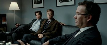 Movie still from “The Ghost Writer” (2010), directed by Roman Polanski – A group of men sitting next to each other on top of a couch; Medium shot, Over the shoulder angle