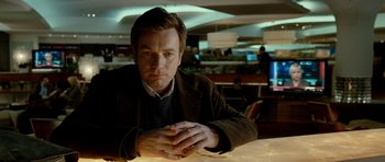 Movie still from “The Ghost Writer” (2010), directed by Roman Polanski – A man sitting at a table with his hands crossed; Medium shot, Low angle