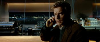 Movie still from “The Ghost Writer” (2010), directed by Roman Polanski – A man is talking on a cell phone in front of an airport window; Close Up shot, Low angle