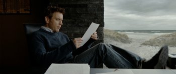 Movie still from “The Ghost Writer” (2010), directed by Roman Polanski – A man sitting on the ground looking at a piece of paper; Medium shot, Low angle