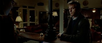 Movie still from “The Ghost Writer” (2010), directed by Roman Polanski – A man sitting at a table in front of a lamp; Medium shot, Over the shoulder angle