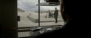 Movie still from “The Ghost Writer” (2010), directed by Roman Polanski – A man in a suit and tie standing in front of an open window; Wide shot, Over the shoulder angle
