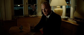 Movie still from “The Ghost Writer” (2010), directed by Roman Polanski – An older man sitting at a table holding a glass of wine; Medium shot, Low angle