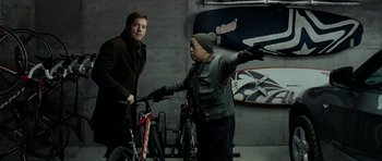 Movie still from “The Ghost Writer” (2010), directed by Roman Polanski – Two men standing next to bicycles in a garage; Medium shot, Over the shoulder angle