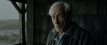 Movie still from “The Ghost Writer” (2010), directed by Roman Polanski – An old man with a gray beard looking at the camera; Close Up shot, Over the shoulder angle
