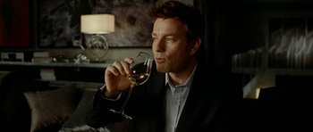 Movie still from “The Ghost Writer” (2010), directed by Roman Polanski – A man holding a glass of white wine in his right hand; Close Up shot, Over the shoulder angle