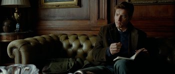 Movie still from “The Ghost Writer” (2010), directed by Roman Polanski – A man sitting on top of a couch in a living room; Medium shot, Over the shoulder angle