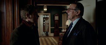 Movie still from “The Ghost Writer” (2010), directed by Roman Polanski – Two men in suits talking in front of a grandfather clock; Medium shot, Over the shoulder angle