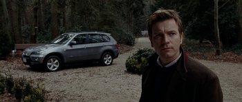 Movie still from “The Ghost Writer” (2010), directed by Roman Polanski – A man standing in front of a car on a gravel road; Medium shot, Over the shoulder angle