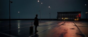 Movie still from “The Ghost Writer” (2010), directed by Roman Polanski – A man standing on the side of a road with a suitcase; Extreme Wide shot, Low angle