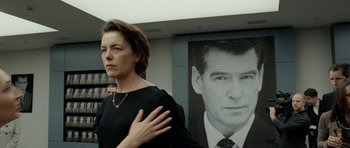 Movie still from “The Ghost Writer” (2010), directed by Roman Polanski – A woman standing in front of a picture of a man in a suit; Medium shot, Over the shoulder angle