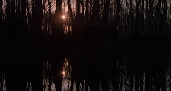 Movie still from “The Gift” (2000), directed by Sam Raimi – A body of water surrounded by trees with the sun setting in the background; Extreme Wide shot, Low angle