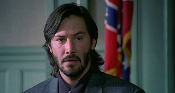 Movie still from “The Gift” (2000), directed by Sam Raimi – A man with long hair and a suit and tie in front of a confederate flag; Close Up shot, Low angle