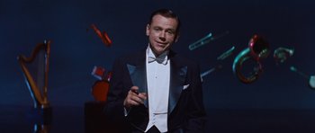 Movie still from “The Girl Can't Help It” (1956), directed by Frank Tashlin – A man in a tuxedo is smoking a cigarette; Medium shot, Low angle