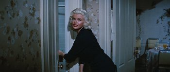 Movie still from “The Girl Can't Help It” (1956), directed by Frank Tashlin – A woman in a black dress leaning against a door; Medium shot, High angle