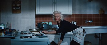 Movie still from “The Girl Can't Help It” (1956), directed by Frank Tashlin – A woman in a black shirt is putting something on a plate; Medium shot, Low angle