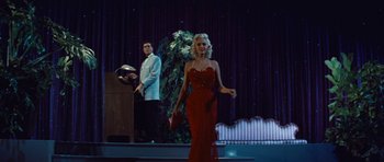 Movie still from “The Girl Can't Help It” (1956), directed by Frank Tashlin – A woman in a red dress on a stage with a man; Wide shot, Low angle