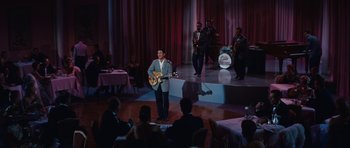 Movie still from “The Girl Can't Help It” (1956), directed by Frank Tashlin – A man in a suit playing a guitar on stage; Extreme Wide shot, High angle