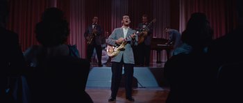 Movie still from “The Girl Can't Help It” (1956), directed by Frank Tashlin – A man in a suit and tie playing a guitar in front of a group of people; Wide shot, High angle
