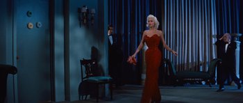 Movie still from “The Girl Can't Help It” (1956), directed by Frank Tashlin – A woman in a red dress holding a red purse in front of a man in a black suit; Wide shot, Low angle