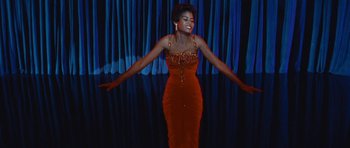 Movie still from “The Girl Can't Help It” (1956), directed by Frank Tashlin – A woman in a red dress standing in front of a blue curtain; Medium shot, Low angle