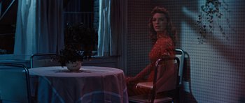 Movie still from “The Girl Can't Help It” (1956), directed by Frank Tashlin – A woman in a red dress sitting at a table in front of a potted plant; Medium shot, Over the shoulder angle