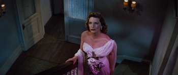 Movie still from “The Girl Can't Help It” (1956), directed by Frank Tashlin – A woman in a pink dress sitting on a stair rail; Medium shot, Low angle